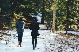 Two people walking on a trail in the woods in winter